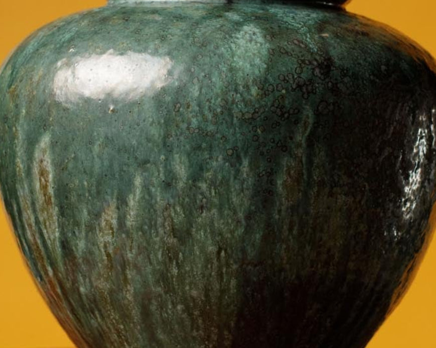 Green marbleized vase on a wooden stand against an orange background